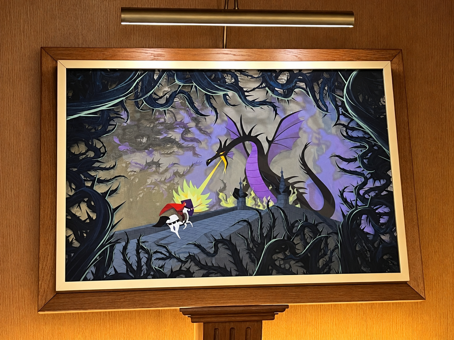 Illustration encadrée représentant le prince Philippe affrontant Maléfique transformée en dragon, au milieu de ronces noires, dans une scène de La Belle au bois dormant.
