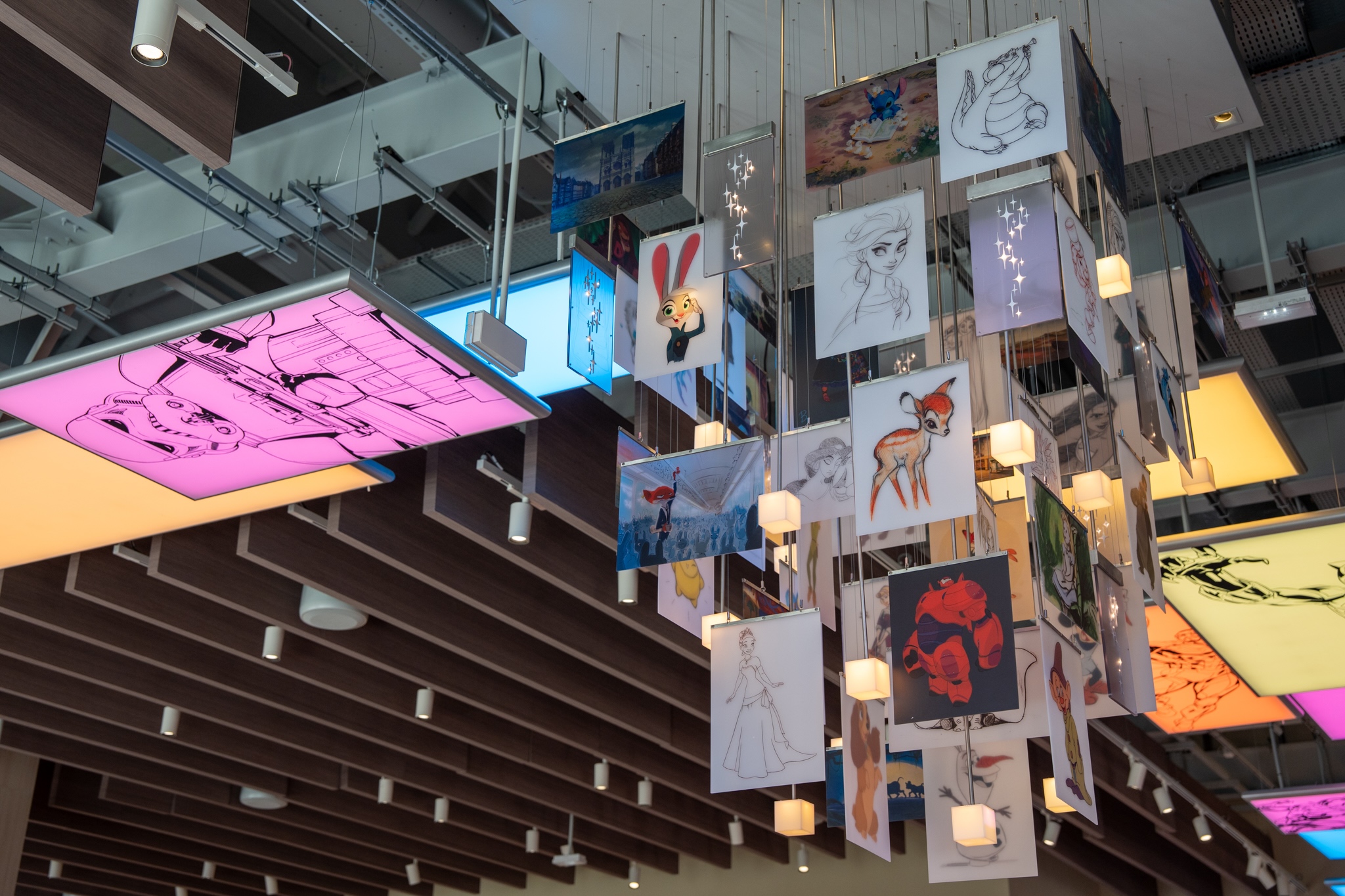 A suspended chandelier featuring panels with Disney characters, including Elsa, Bambi, Judy Hopps, and Baymax, combining concept sketches, colorful illustrations, and illuminated cubes.