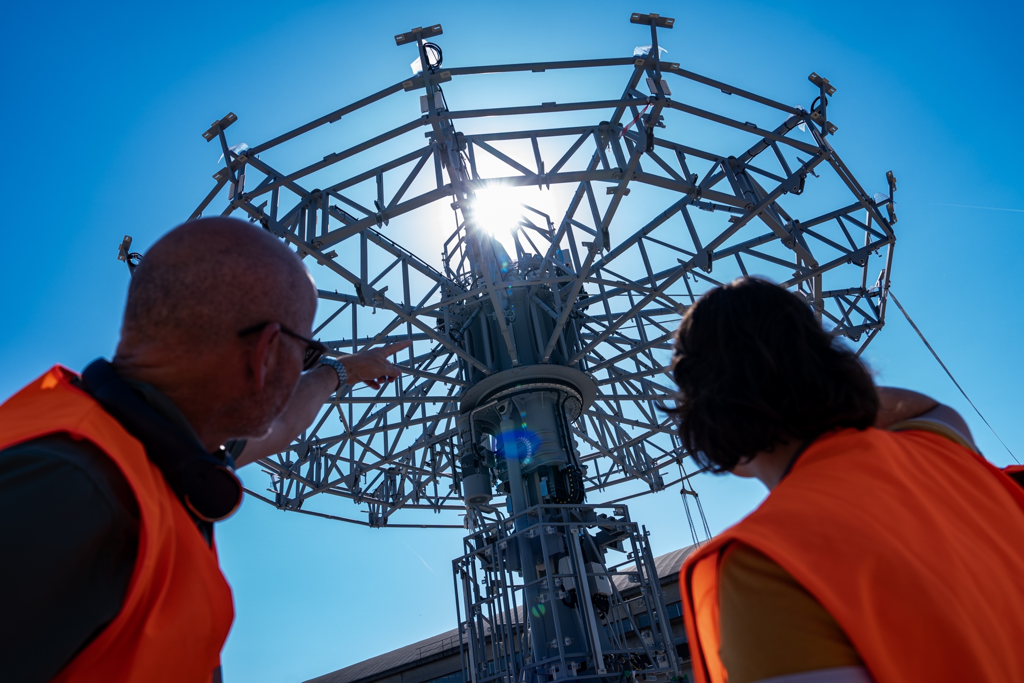 Deux membres des équipes techniques, vêtus de gilets de sécurité orange, observent la structure métallique de la future attraction Wilderness Explorers Sky Swings à Disney Adventure World.